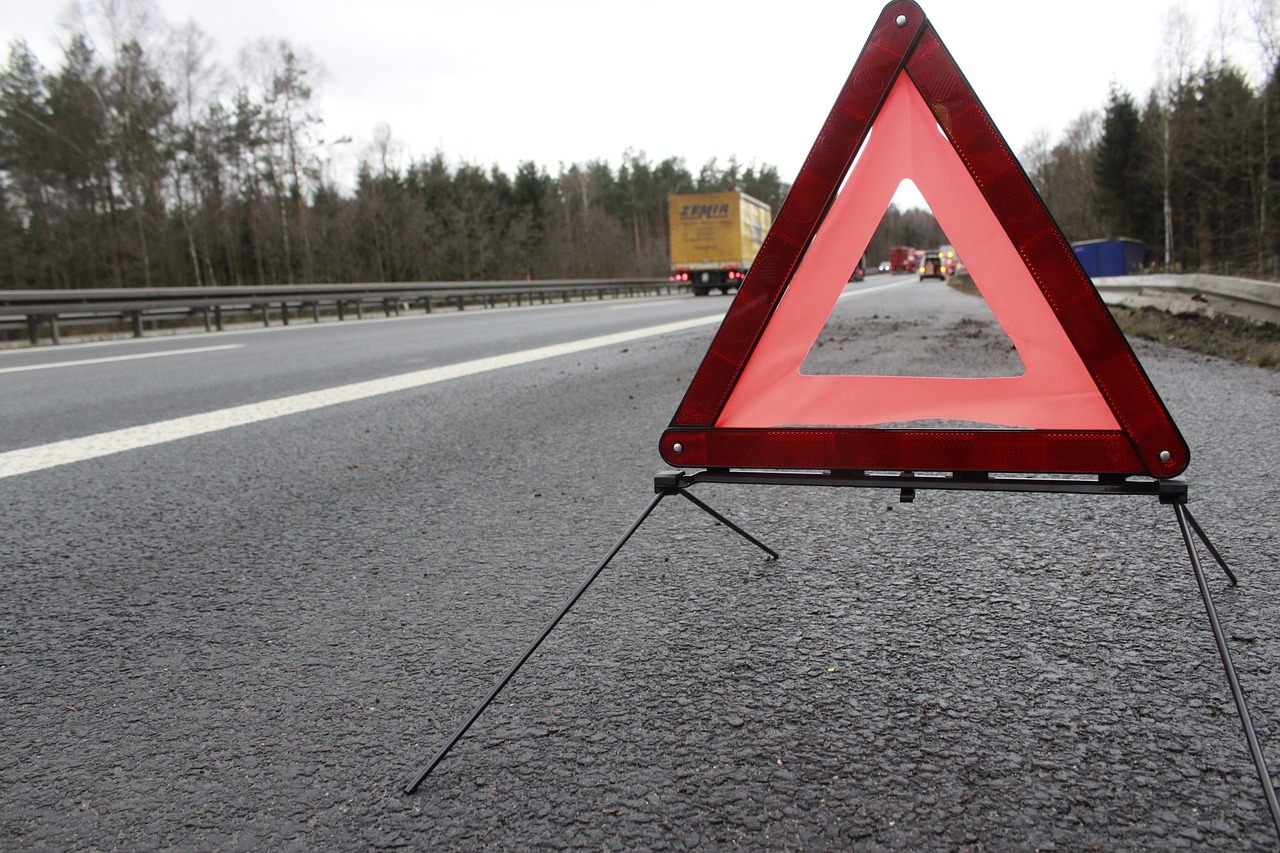 Sigurnosni upozoravajući trougao postavljen na asfaltu autoputa s prometom i šumom u pozadini.